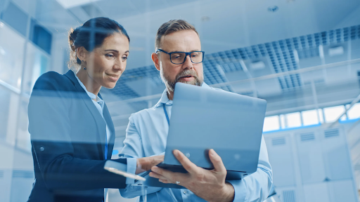 homem e mulher em ambiente corporativo observam a tela de um notebook.